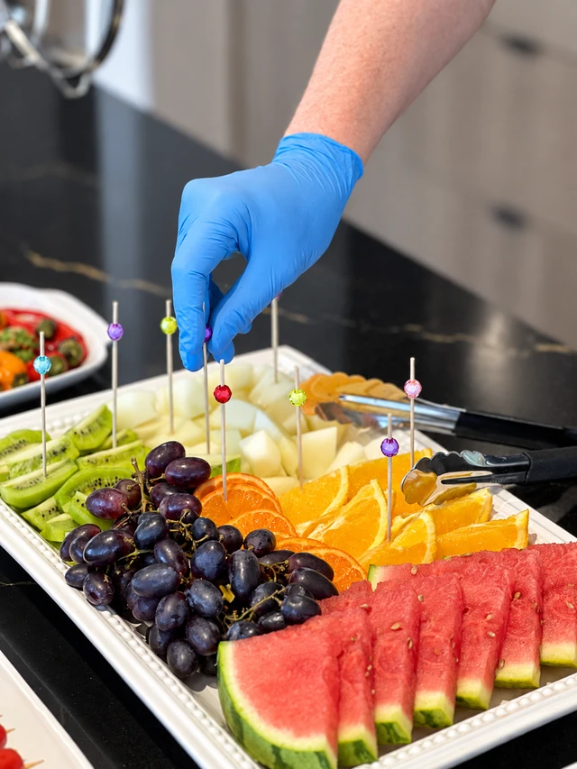 A gloved hand arranging the fruit and cheese platter at a buffet